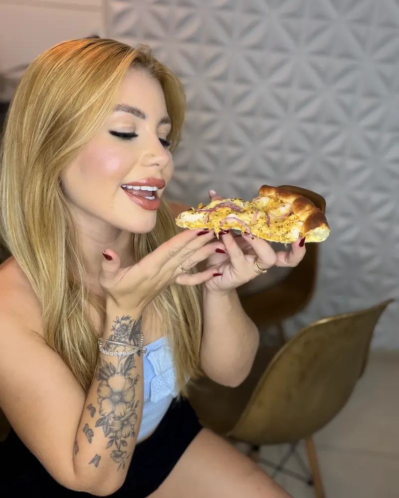 Bell sorrindo e comendo um salgado em um estúdio claro