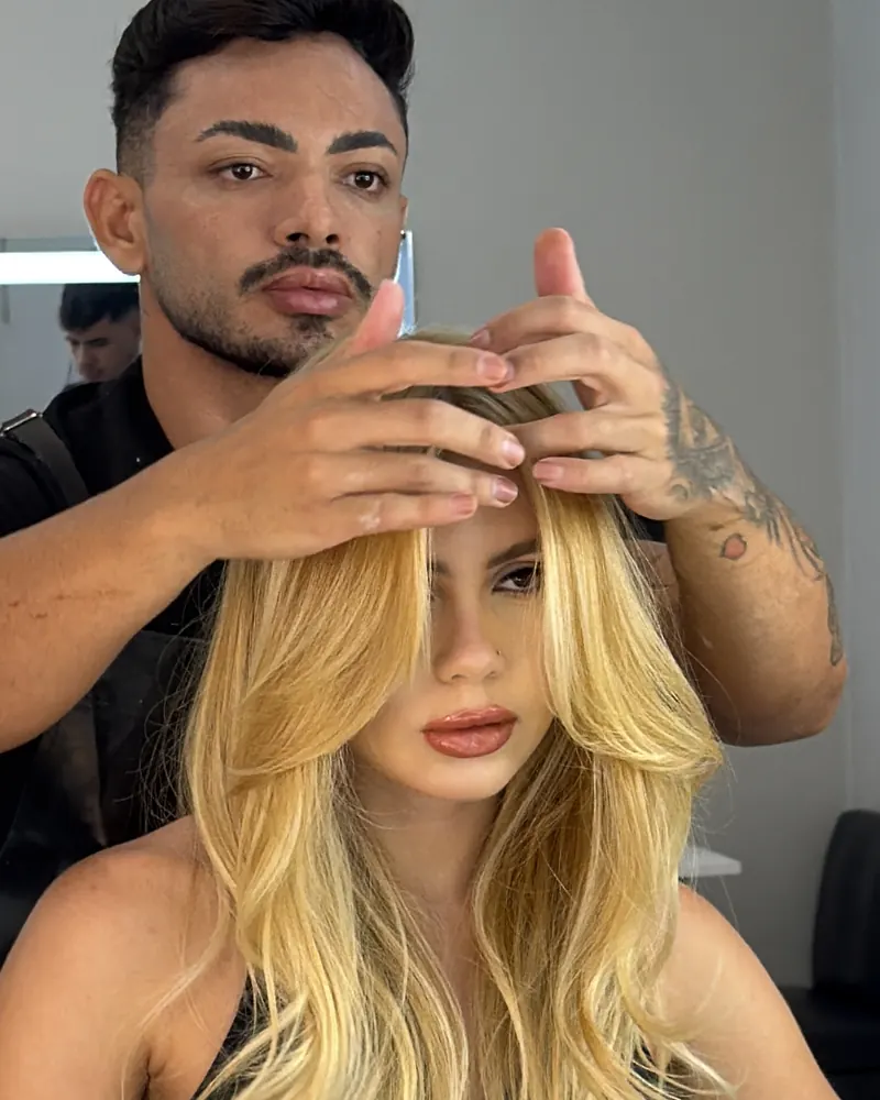 Bell sentada em um salão, com o cabelo loiro sendo ajeitado